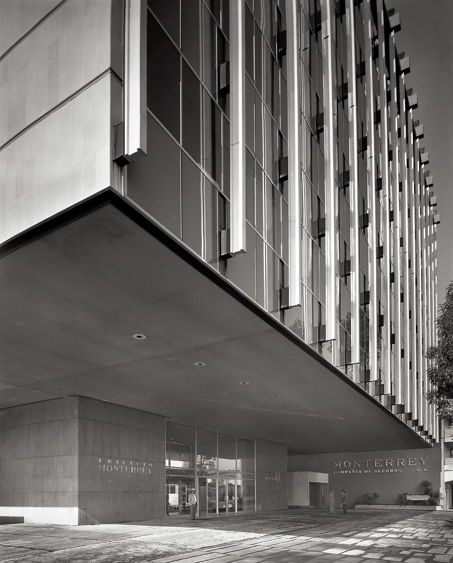 Vista de los apoyos del edificio y plaza de acceso. En la fachada se aprecian los tensores exteriores, sujetando las trabes de celosía en cada piso. (AGP 72-100, AAM-FA/UNAM)